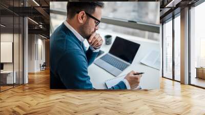 Serious young adult businessman or entrepreneur, taking notes in his notebook at the office. Wall mural