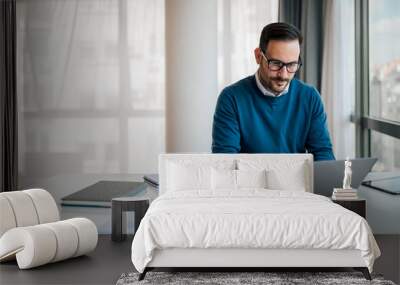 Serious young male professional working on laptop while sitting at office Wall mural