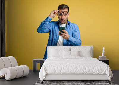 Shocked businessman reading unexpected message over smart phone against yellow background Wall mural