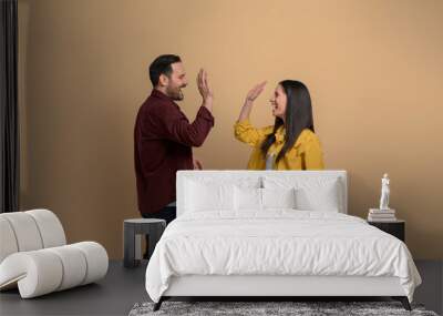 Side view of cheerful boyfriend and girlfriend giving high-five to each other and screaming over beige background. Excited young couple clapping hands and celebrating success Wall mural