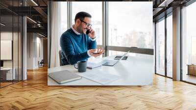 Smiling entrepreneur discussing on cellphone while using laptop. Wall mural