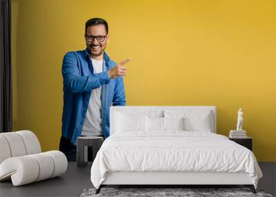 Smiling male entrepreneur pointing at copy space for marketing while standing on yellow background Wall mural