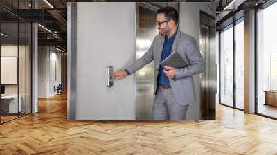 Smiling male financial advisor with laptop pushing button and waiting for elevator in modern office Wall mural