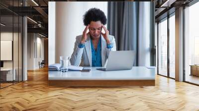 Stressed businesswoman having headache while using laptop at desk in office Wall mural