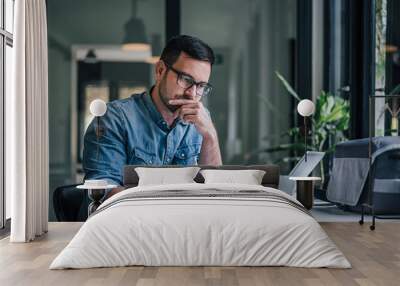 Thoughtful entrepreneur making notes while working on laptop in home office Wall mural