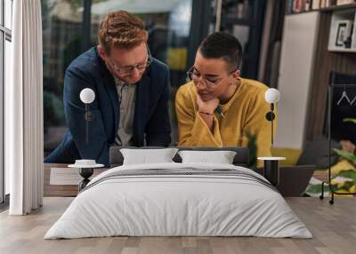 Two diverse natural colleagues in casual office or home office doing paperwork working together teaching, coaching or tutoring each other one another Wall mural