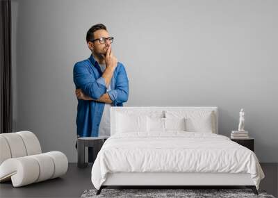 Young male entrepreneur with hand on chin thinking business ideas while standing on white background Wall mural