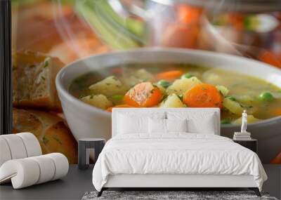 A bowl of soup with carrots and peas sits on a table next to a piece of bread Wall mural