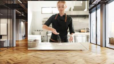 Medium shot of the hands of a woman who sprinkles flour on the table surface in slow motion against the background of a black apron. The process of preparing dough on the production floor in a bakery. Wall mural