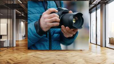 Close-up of a person holding a DSLR camera while wearing a blue jacket, suggesting outdoor photography in colder weather. Wall mural