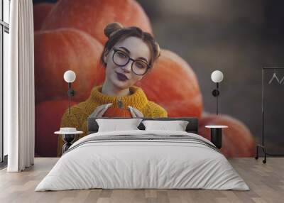 Cozy autumn photo of a girl with pumpkins in a yellow sweater and glasses. Stylish young woman in autumn decorations holding a small pumpkin. Wall mural