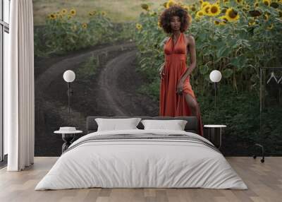 Young black woman in a long orange dress walks in the sunflower field. Wall mural