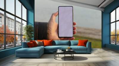 Mock up - man holding smart phone with clean white screen by the lake in nature Wall mural