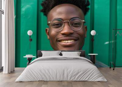 Confident young man with stylish glasses, smiling in casual attire on green background Wall mural