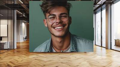 Confident young man with stylish glasses, smiling in casual attire on green background Wall mural