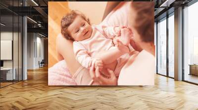 Sleepy funny baby girl under 1 year old lying in bed on mother hands closeup in room. Looking at each other. Childhood. Motherhood. Wall mural