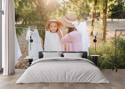 Two child girls playing having fun hanging white bed sheets on rope outdoor. Childhood. Friendship. Wall mural