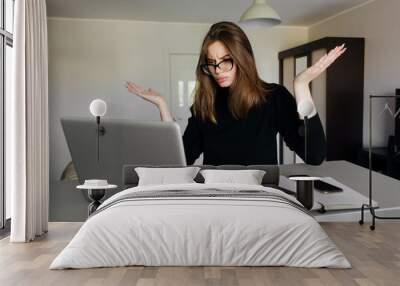 Beautiful young woman working using computer clueless and confused expression with arms and hands raised. Doubt concept. Wall mural