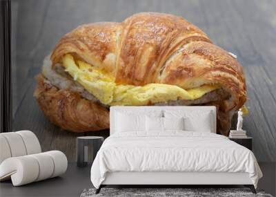 Delicious croissant sandwich loaded with scrambled eggs, melted cheese, and sausage patty for a complete meal. Wall mural