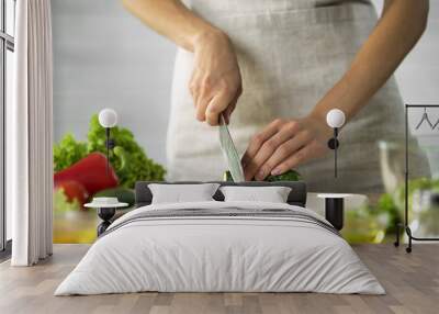 Female chef slicing fresh cucumber with a knife on wooden board, vegetables Wall mural