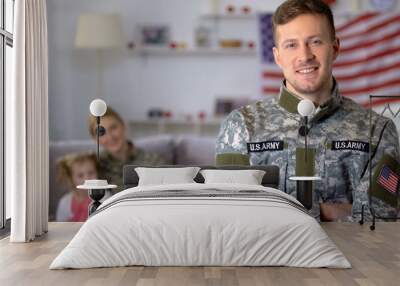 Happy male veteran of US army smiling at camera, wife and daughter on background Wall mural