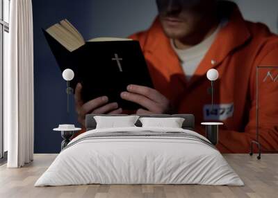 Imprisoned man in handcuffs reading bible, feeling guilty and praying for soul Wall mural