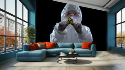 Scientist in protective suit showing ionizing radiation sign, black background Wall mural