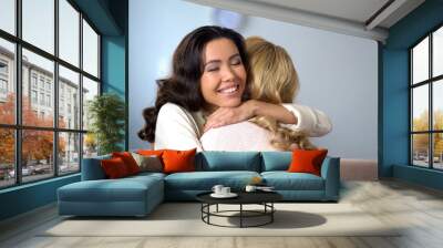 Two beautiful women hugging and smiling, true old friends meeting, indoors Wall mural