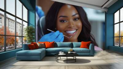 Dentist with blue gloves is holding the dental mirror and smiling beautiful woman in pink top sitting on grey chair near white wall Wall mural