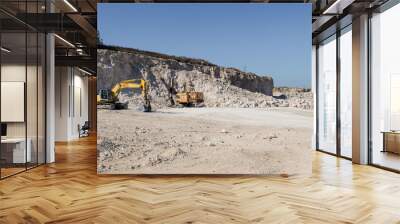 A large yellow tracked excavator is mining rock in a quarry. Wall mural