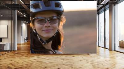 Girl on a mountain bike on offroad, beautiful portrait of a cyclist at sunset, Fitness girl rides a modern carbon fiber mountain bike in sportswear. Close-up portrait of a girl in a helmet and glasses Wall mural