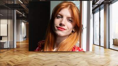 Red-haired young active girl with a smile on her face in a red dress. Classic portrait by the window. Wall mural