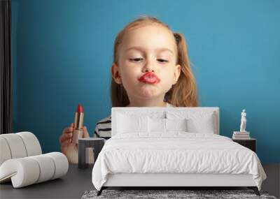 Happy little girl puts lipstick on her lips on blue background. Little trendy. little girl applying makeup Wall mural