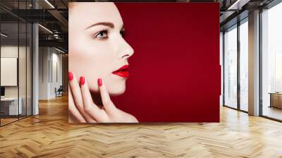 Beautiful model profile closeup beauty shot with red manicured nails and lips. Isolated on red background.  Wall mural