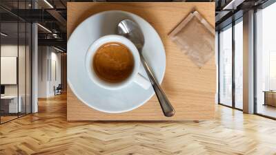 Small italian espresso in white ceramic cup with spoon and packet of sugar isolated on light wood desk from above. Wall mural