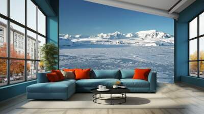 Fly over snowy mountain landscape in Antarctica. Polar frozen ocean landscape covered by snow under blue sunny sky. Discover the beauty of South Pole. Antarctica travel and exploration background Wall mural