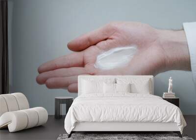 A hand holding a small amount of white cream on a neutral background, ideal for beauty and skincare concepts. Wall mural