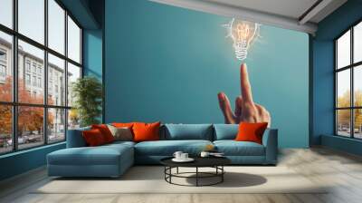 A hand touching a drawn lightbulb symbolizing an idea on a teal background. Wall mural