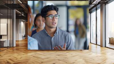 A young man in glasses actively engaging in a discussion at a business meeting. Wall mural