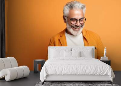 An elderly man smiling and laughing with his phone against a colored background. Wall mural