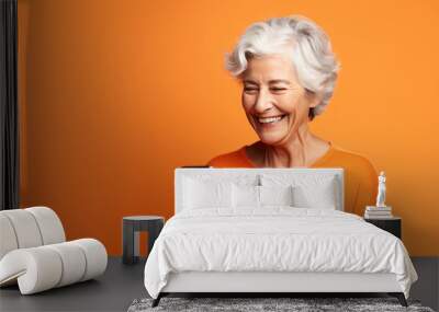 An elderly woman smiling with her phone against an orange background. Wall mural