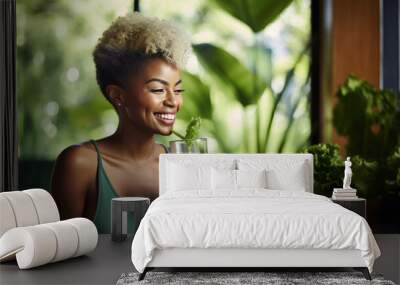 Cheerful young woman with a distinctive hairstyle, holding a green smoothie, standing in front of a blurred background with indoor plants. Wall mural