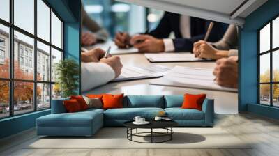 Close-up view of hands signing a document, with multiple individuals engaged in a business meeting around a table. Wall mural