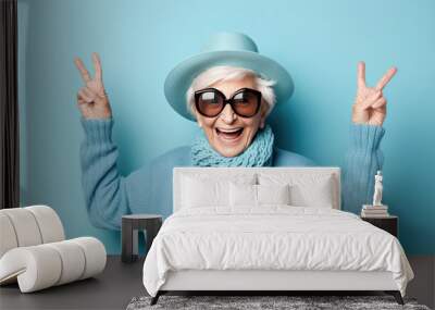 Elderly stylishly dressed woman showing peace sign on fingers on blue background. Wall mural