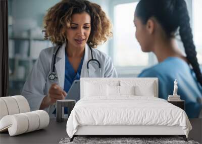 focused female doctor in a white coat with a stethoscope around her neck using a tablet while consulting with a patient or colleague Wall mural