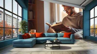 Handsome man reading a book at home.Created with Generative AI technology. Wall mural