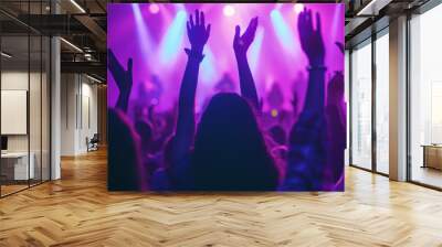 lively crowd at a concert, with hands raised in the air, silhouetted against a backdrop of vibrant stage lights, capturing the energy and excitement of a live music event. Wall mural