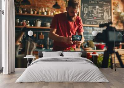 Man is focused on adjusting a camera in a home kitchen setting, with a video setup in the background, suggesting he is filming a cooking tutorial or vlog. Wall mural