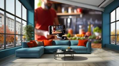 Man is focused on adjusting a camera in a home kitchen setting, with a video setup in the background, suggesting he is filming a cooking tutorial or vlog. Wall mural