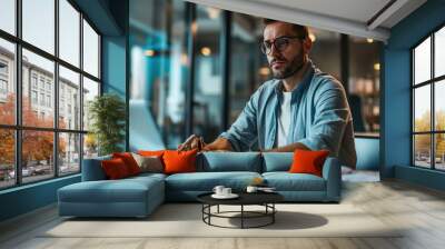 Man smiling while working on a laptop in a modern office environment Wall mural